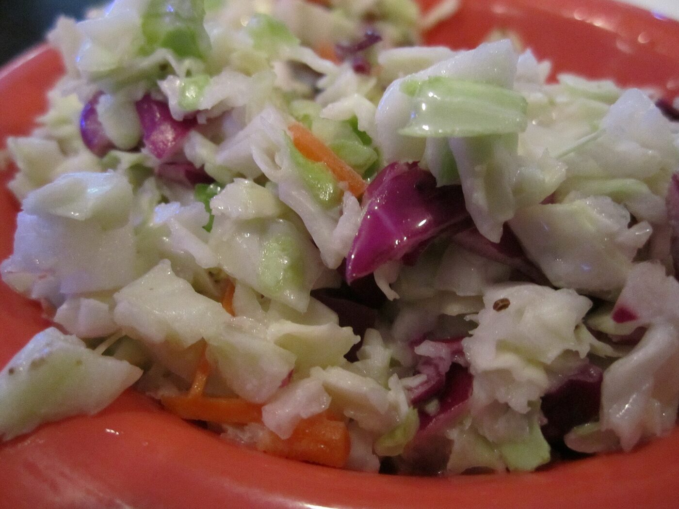Plato naranja con coleslaw: col picada en trozos, zanahoria y col morada, cubierto de mayonesa.
