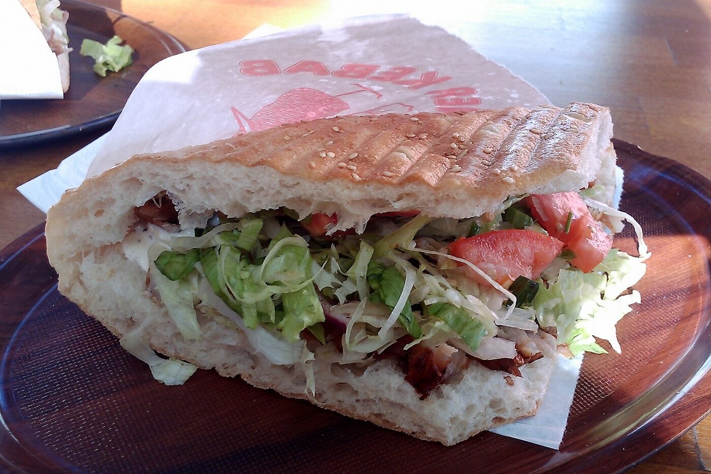 Un Döner Kebab en pan plano tostado con ajonjolí, relleno de carne, lechuga, col y jitomate, sobre papel en un plato café. Berlín, 2010.