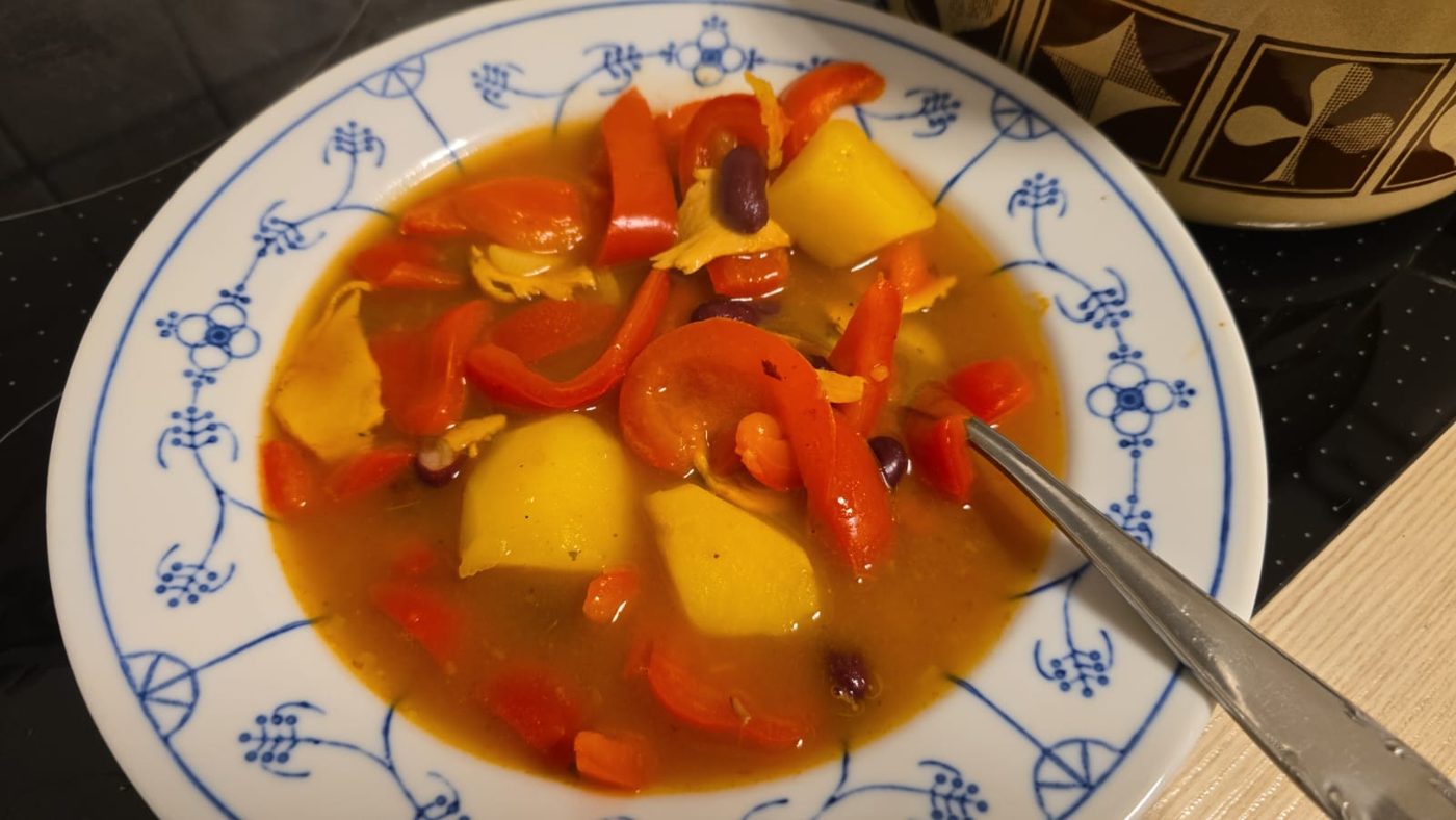 Plato hondo de porcelana azul con un guiso de papa, pimiento rojo y frijol.