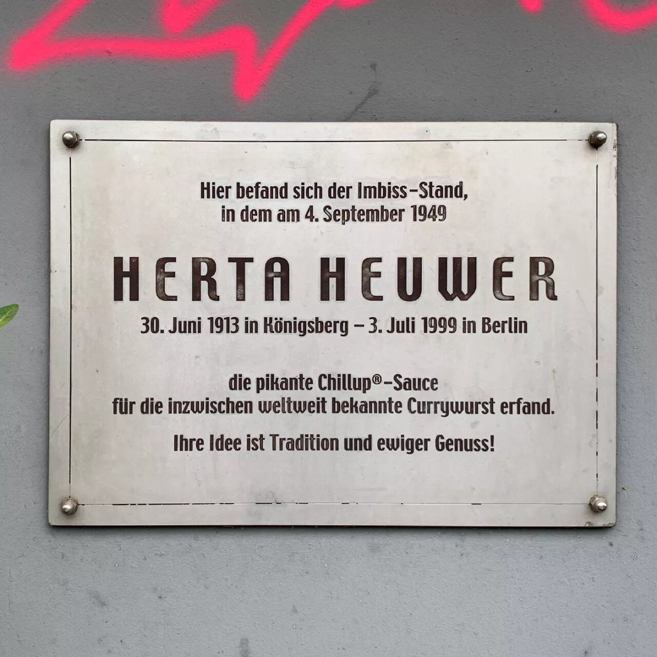 Placa metálica en una pared gris con letras grabadas en alemán que recuerdan a Herta Heuwer y la fecha 4 de septiembre de 1949.