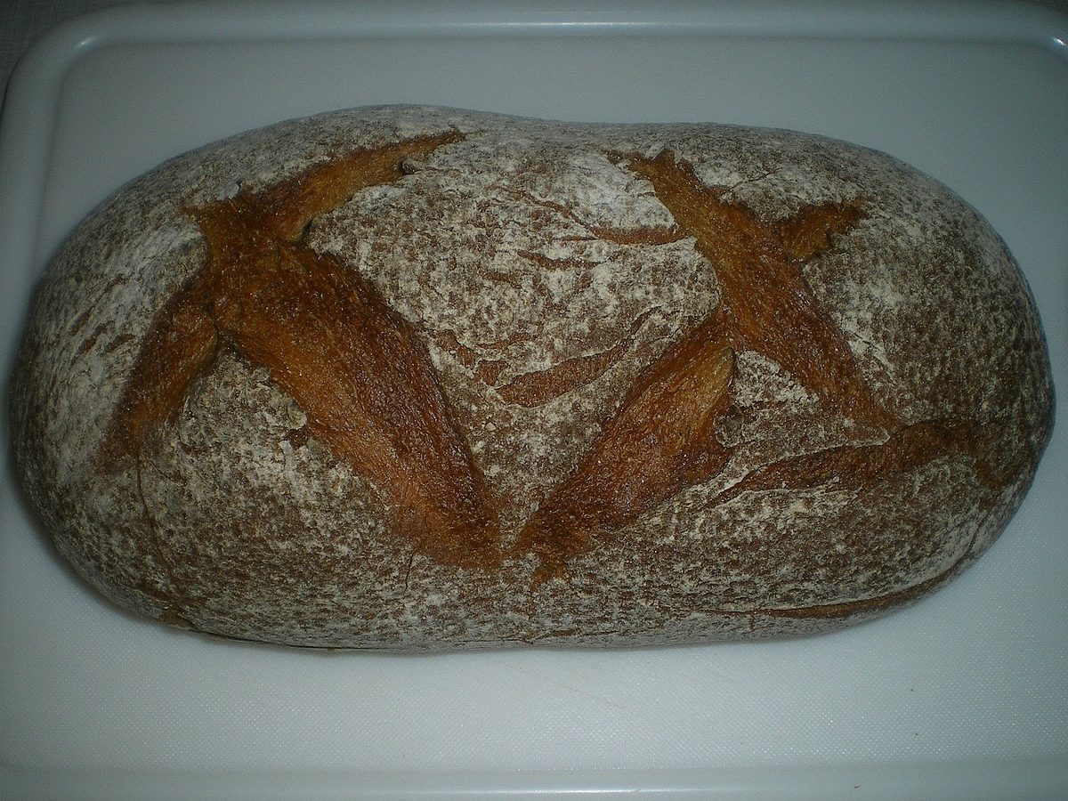 Hogaza ovalada de pan de centeno con corteza enharinada y cortes en forma de espiga.